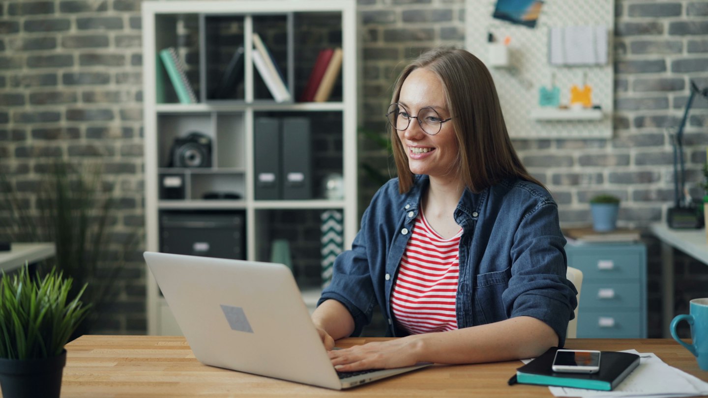 Woman with glasses typing on a laptop at a desk.